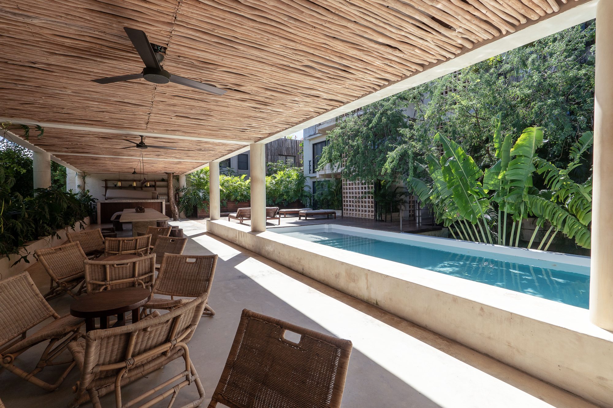 Covered lounge with a woven ceiling, ceiling fans, wicker chairs and a pool