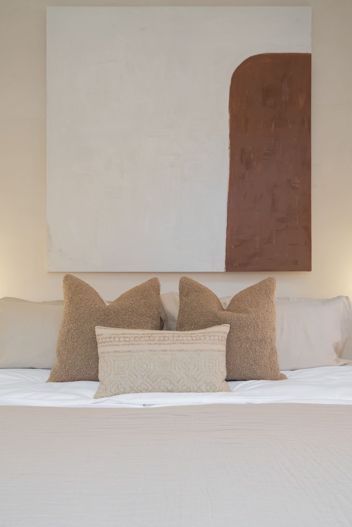 King bed with neutral cushions and terracotta wall art