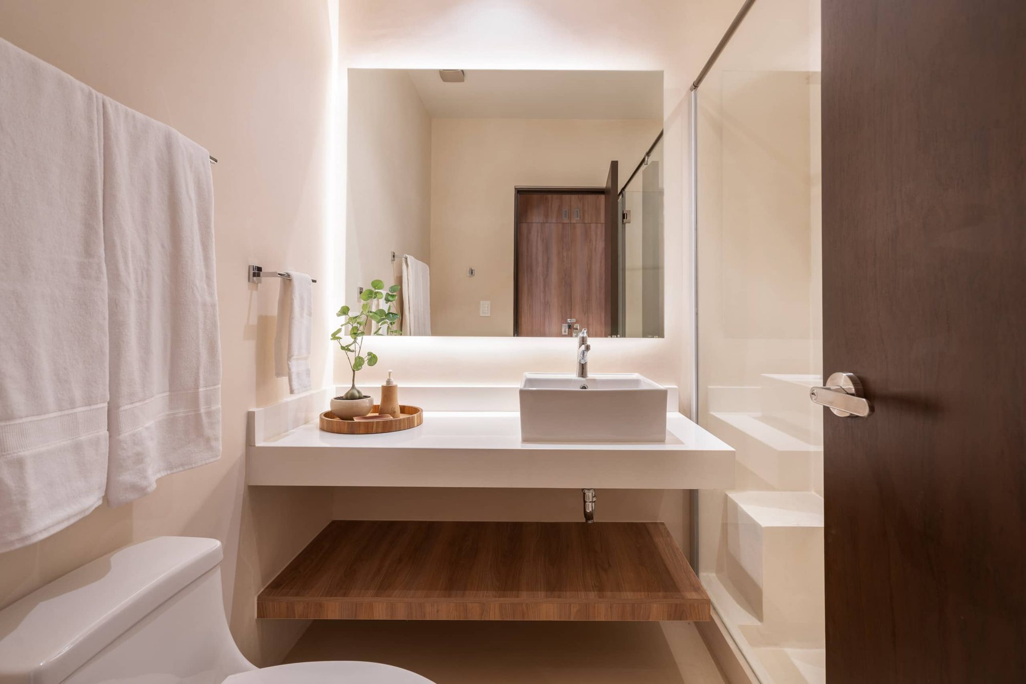 Bathroom with a vessel sink, backlit mirror and floating wood shelf