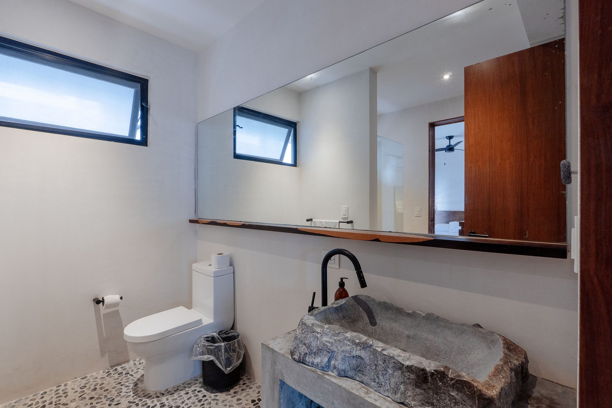 Bathroom with a stone vessel sink, toilet and pebble tile floor