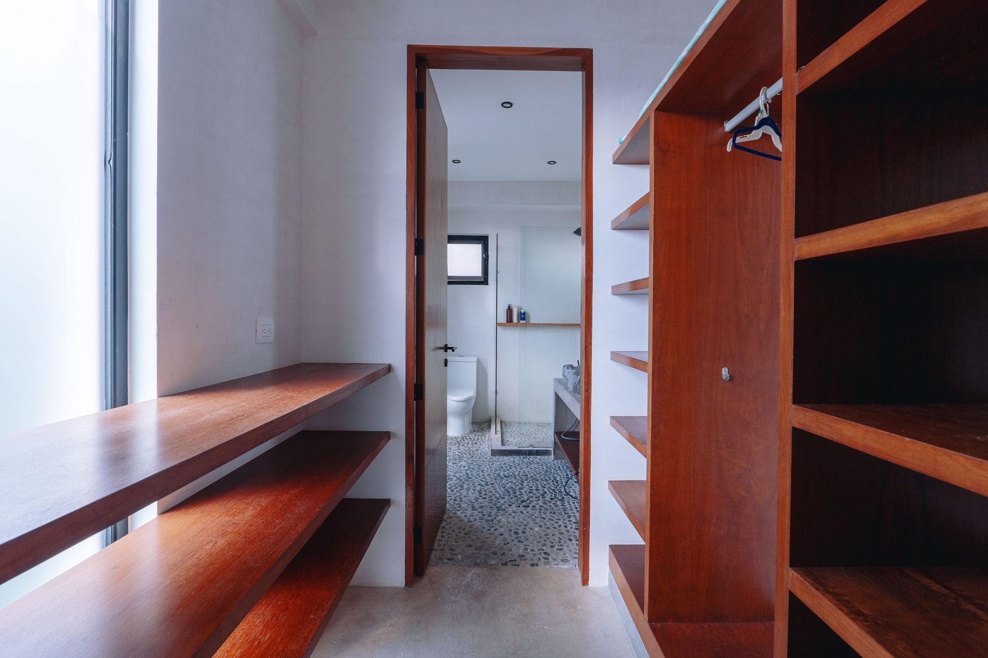 Closet with wooden shelves and hanging rail leading to the bathroom