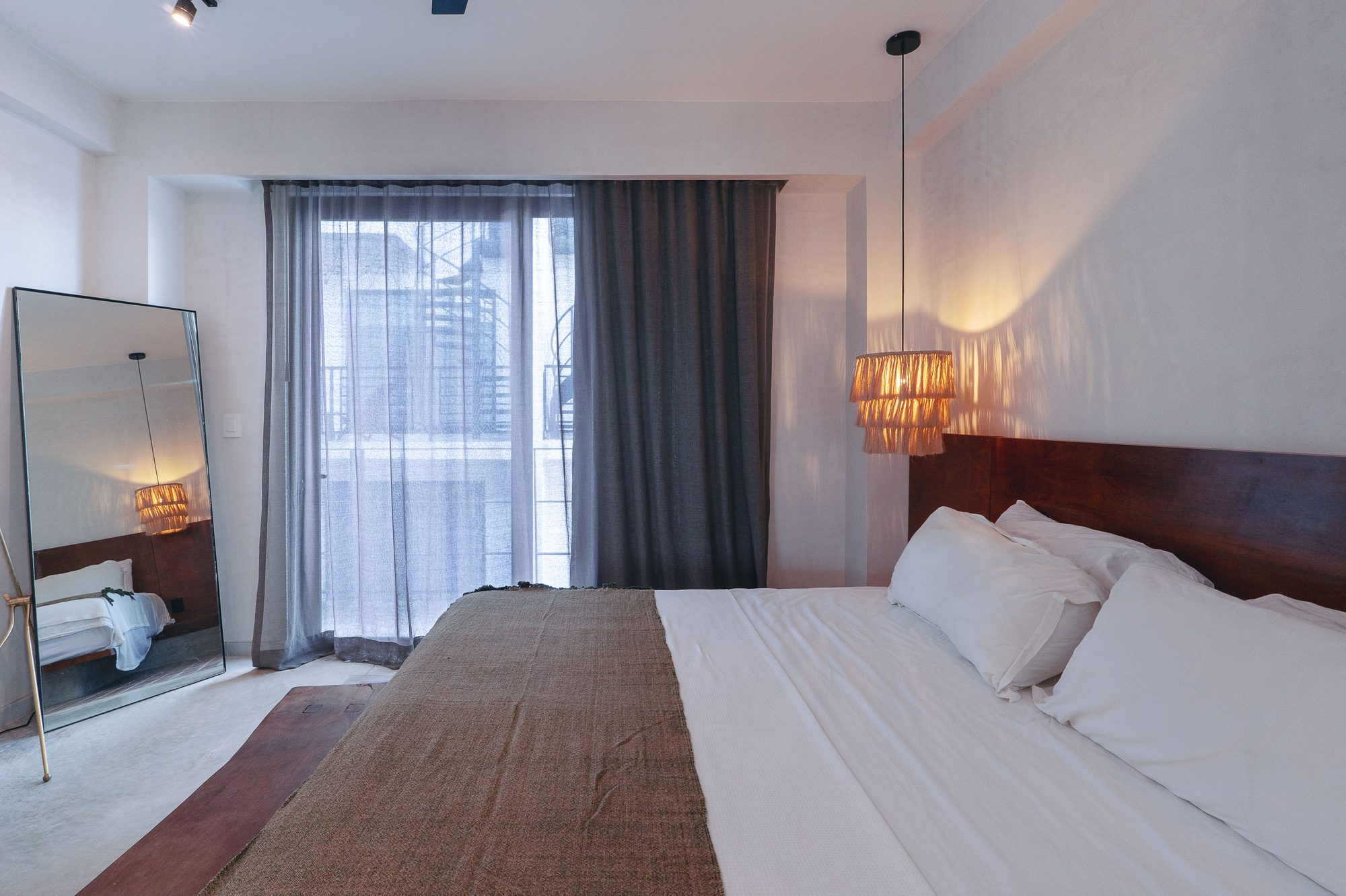 Bedroom with a king bed, woven pendant lights, full-length mirror and curtained window