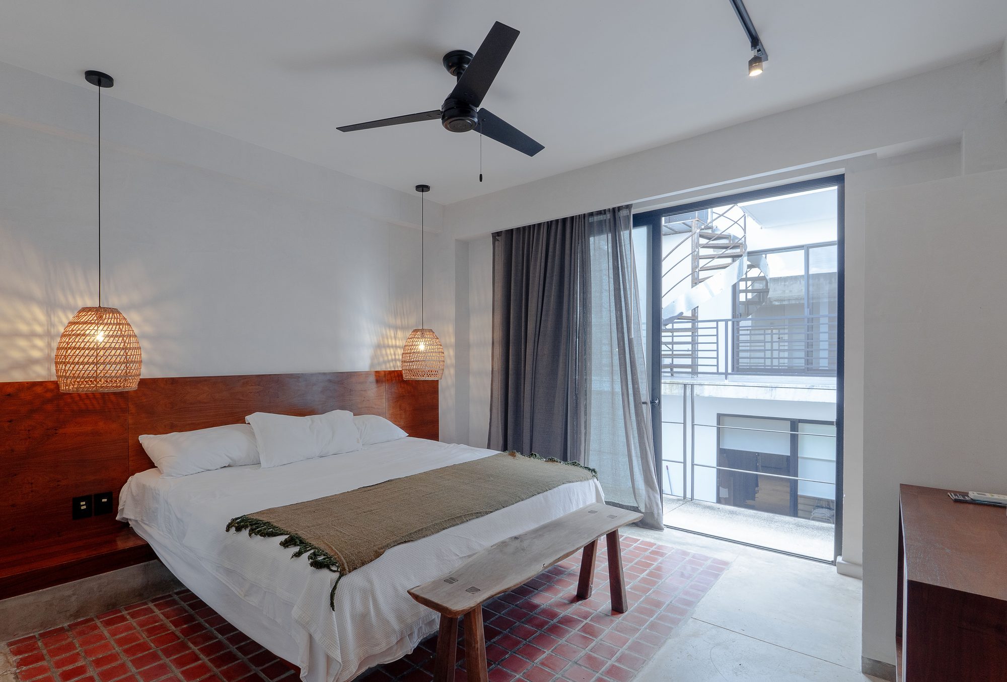 King bed beside a glass door with a ceiling fan and woven pendant lamps