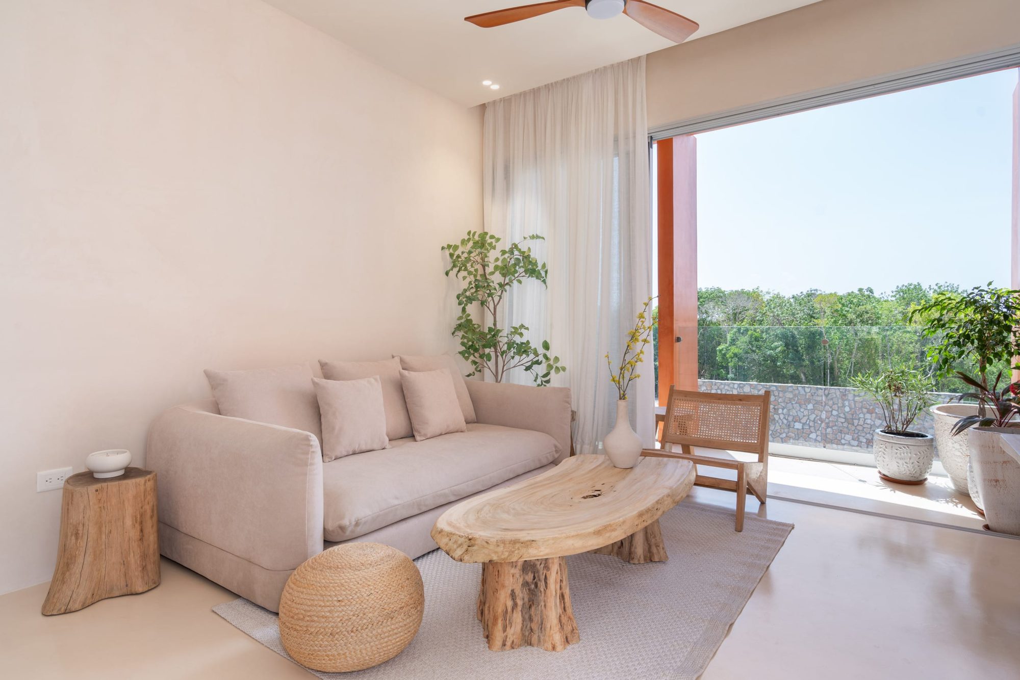 Living room sofa and wood coffee table beside sliding doors to the balcony with treetop views