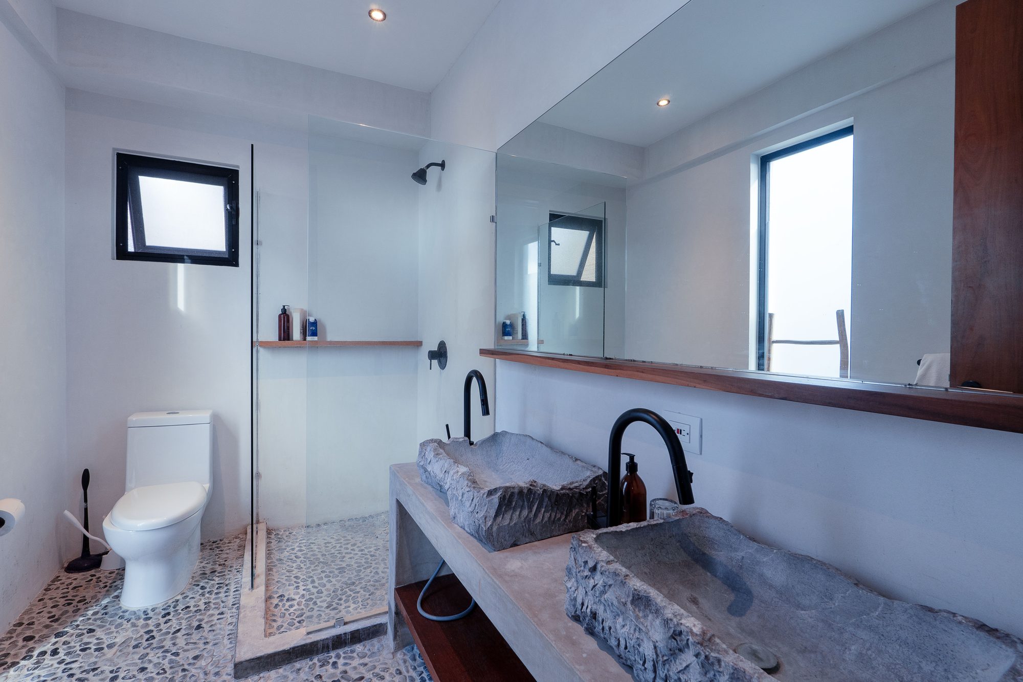 Bathroom with a glass shower, toilet, pebble floor and stone vessel sink