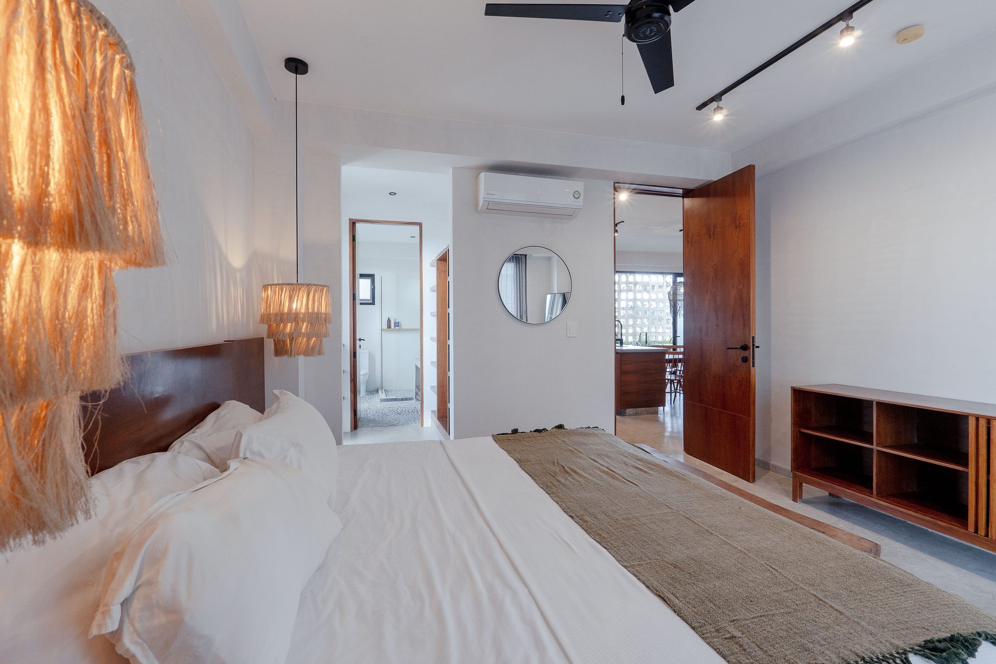 King bedroom with a ceiling fan, round mirror, wood dresser and woven pendant lights